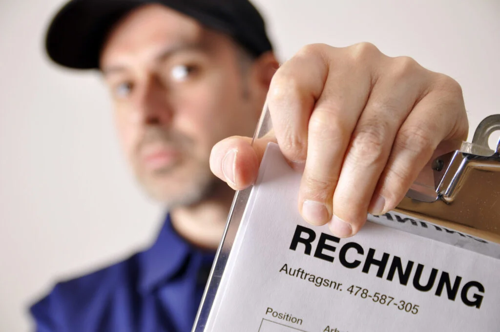 Reverse-Charge-Verfahren im Dachdeckerhandwerk Handwerker prüft eine Rechnung auf einem Klemmbrett
